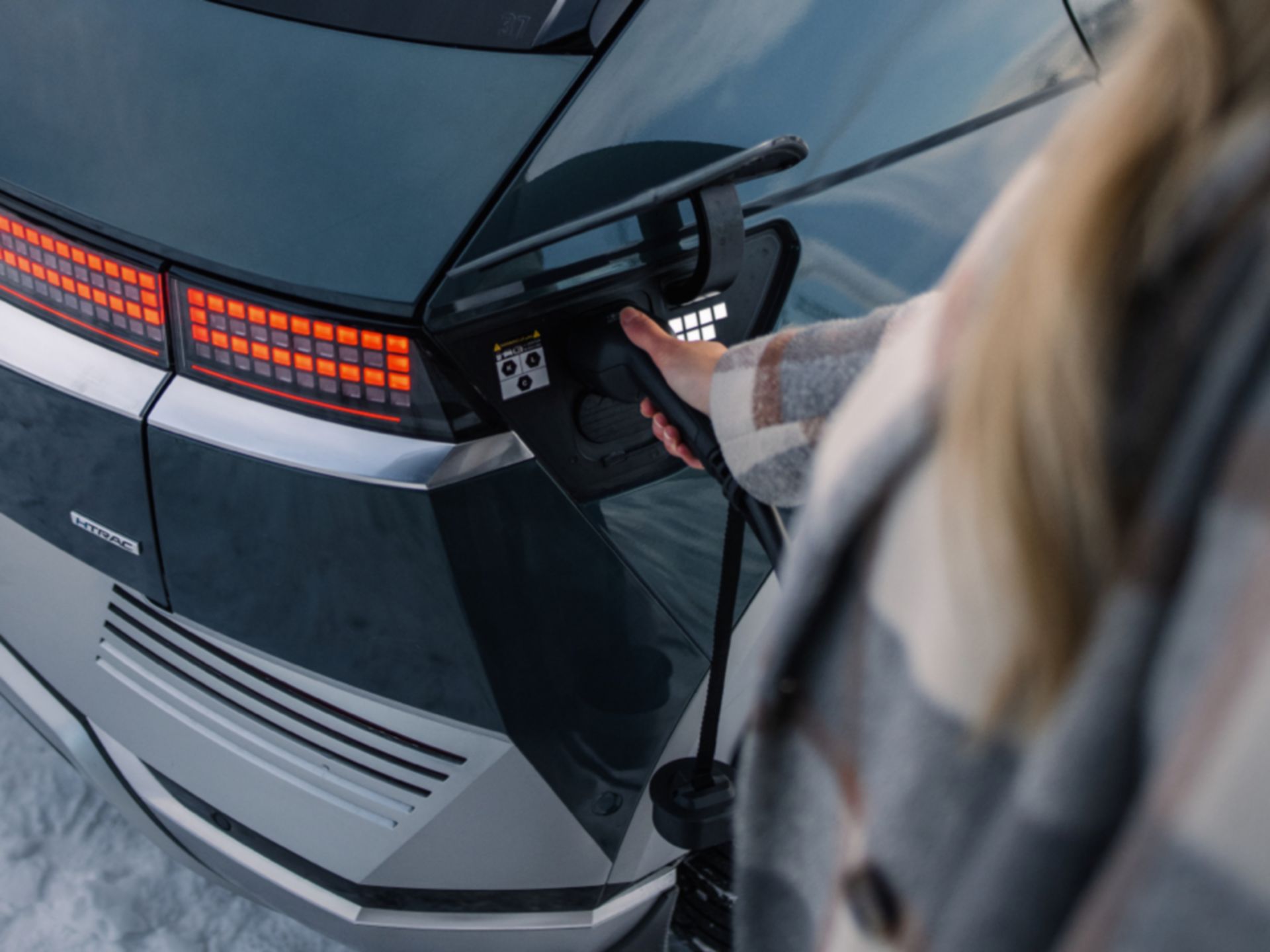 The Hyundai IONIQ 5 electric vehicle getting plugged in to charge by a woman.