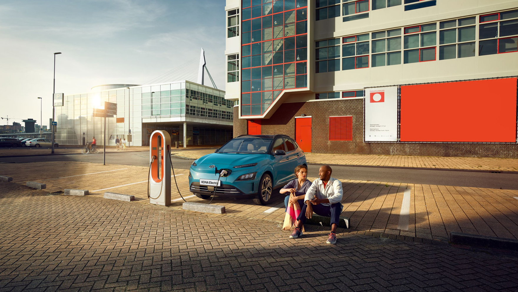 A couple sitting in a parking lot while the new Hyundai Kona Electric is charging on a public charging station. 