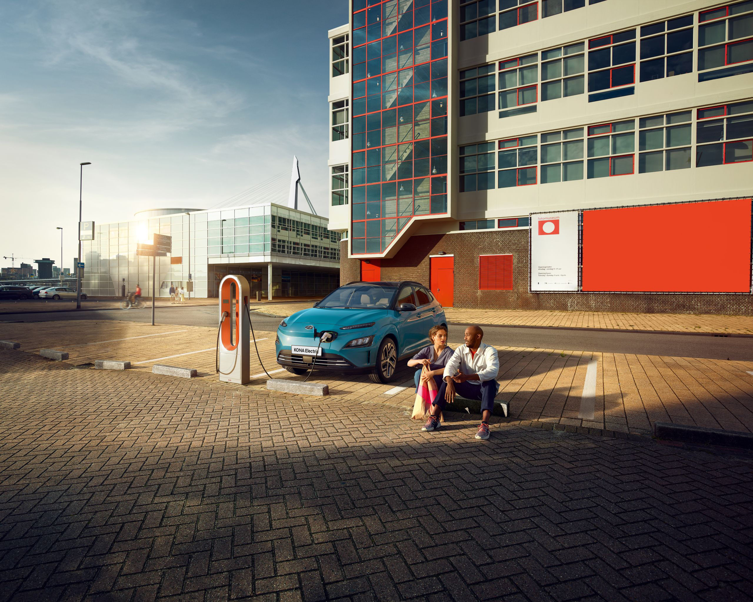 A couple sitting in a parking lot while the new Hyundai Kona Electric is charging on a public charging station. 