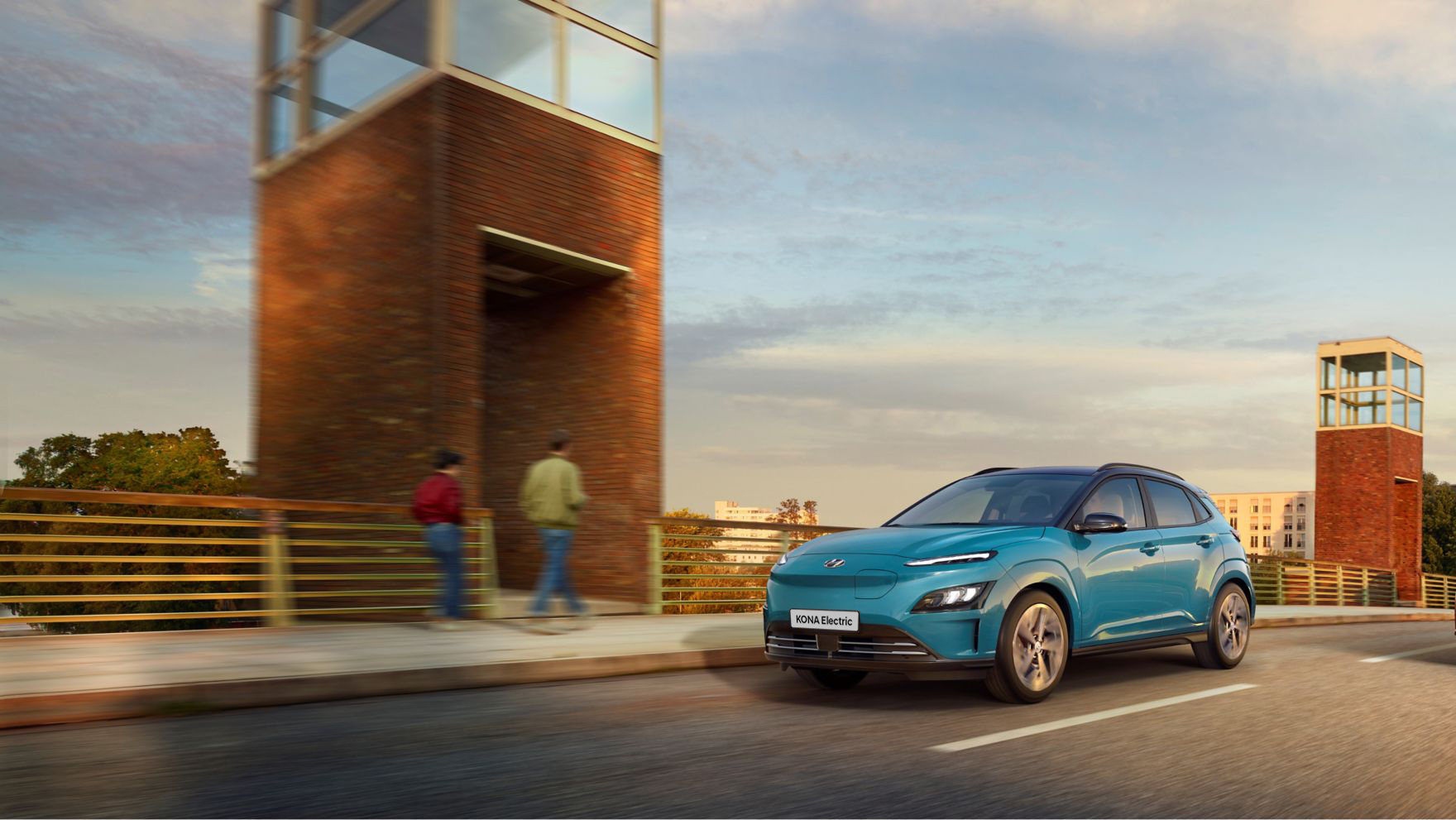 The new Hyundai Kona Electric driving over a bridge in the evening. 