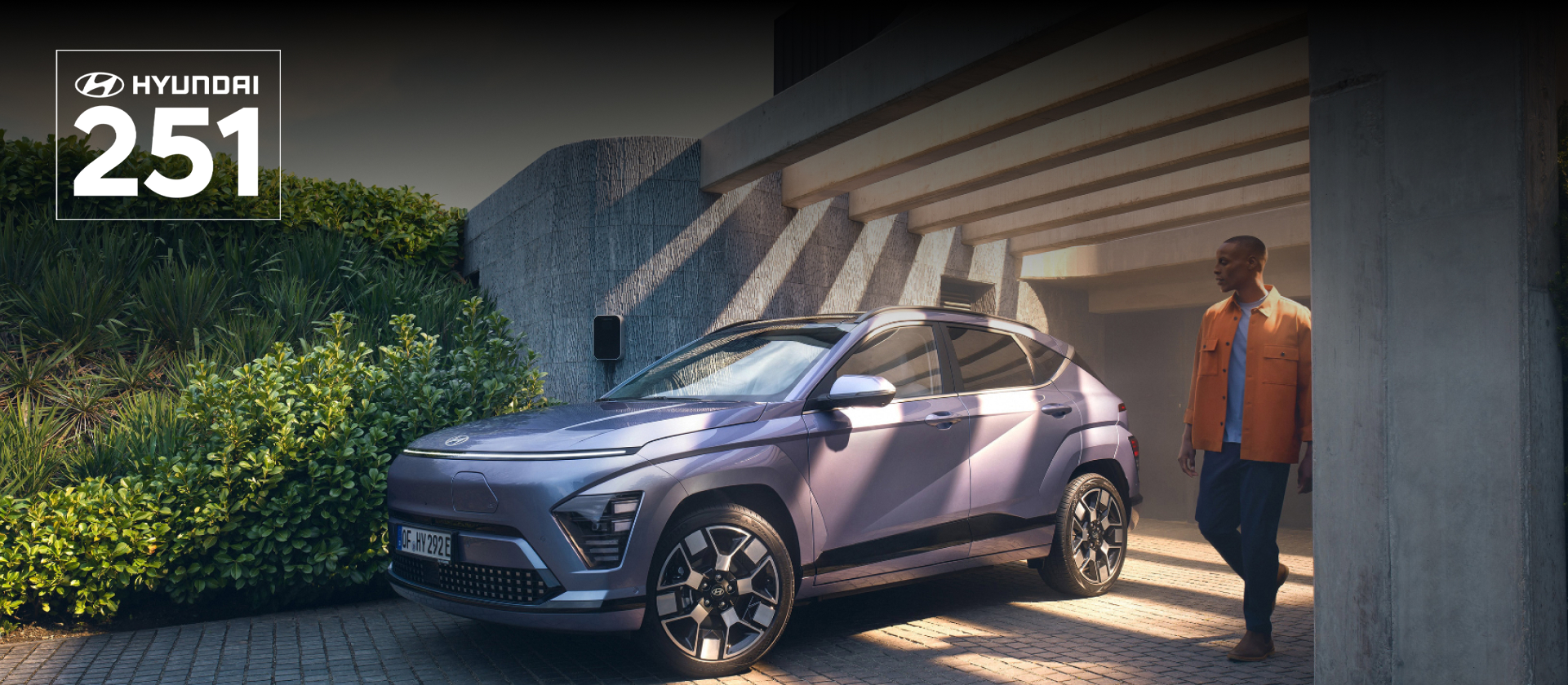 The Hyundai KONA Electric bathed in sunlight with a man walking away from a garage.