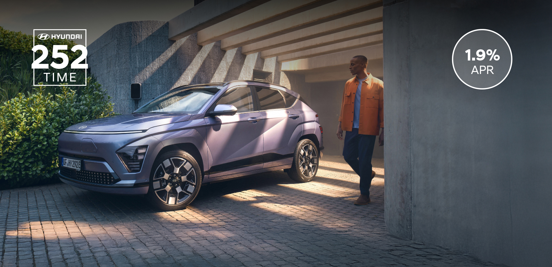 The Hyundai KONA Electric bathed in sunlight with a man walking away from a garage.