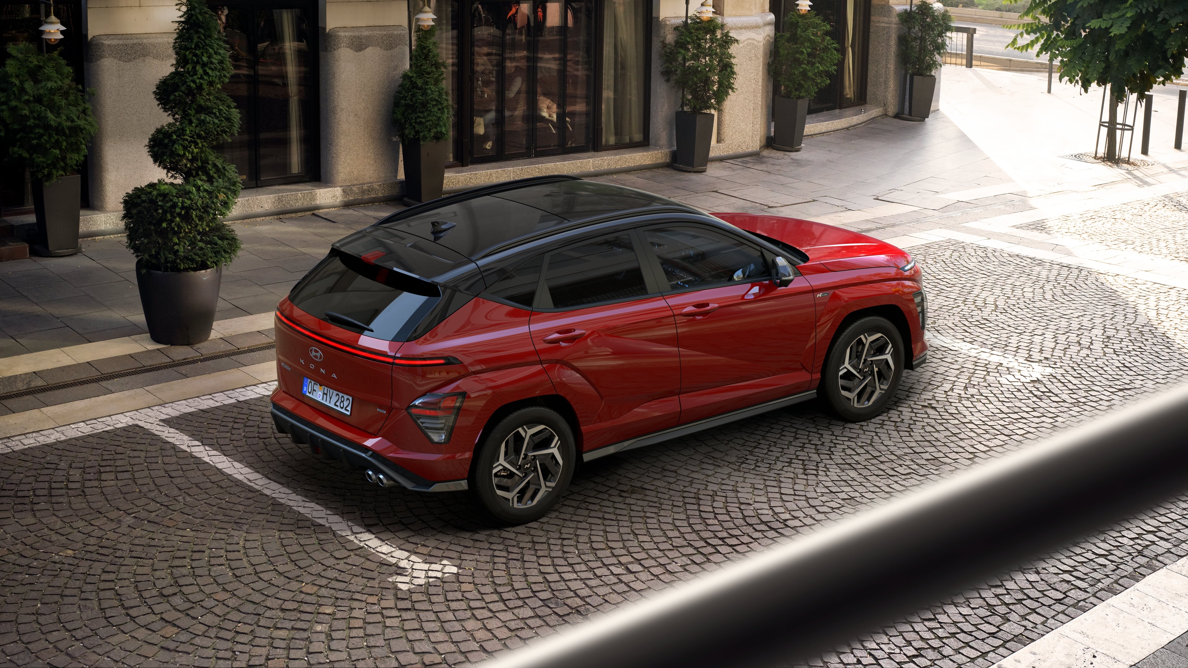 The all-new Hyundai KONA N Line in red parked in front of a building with several small trees.