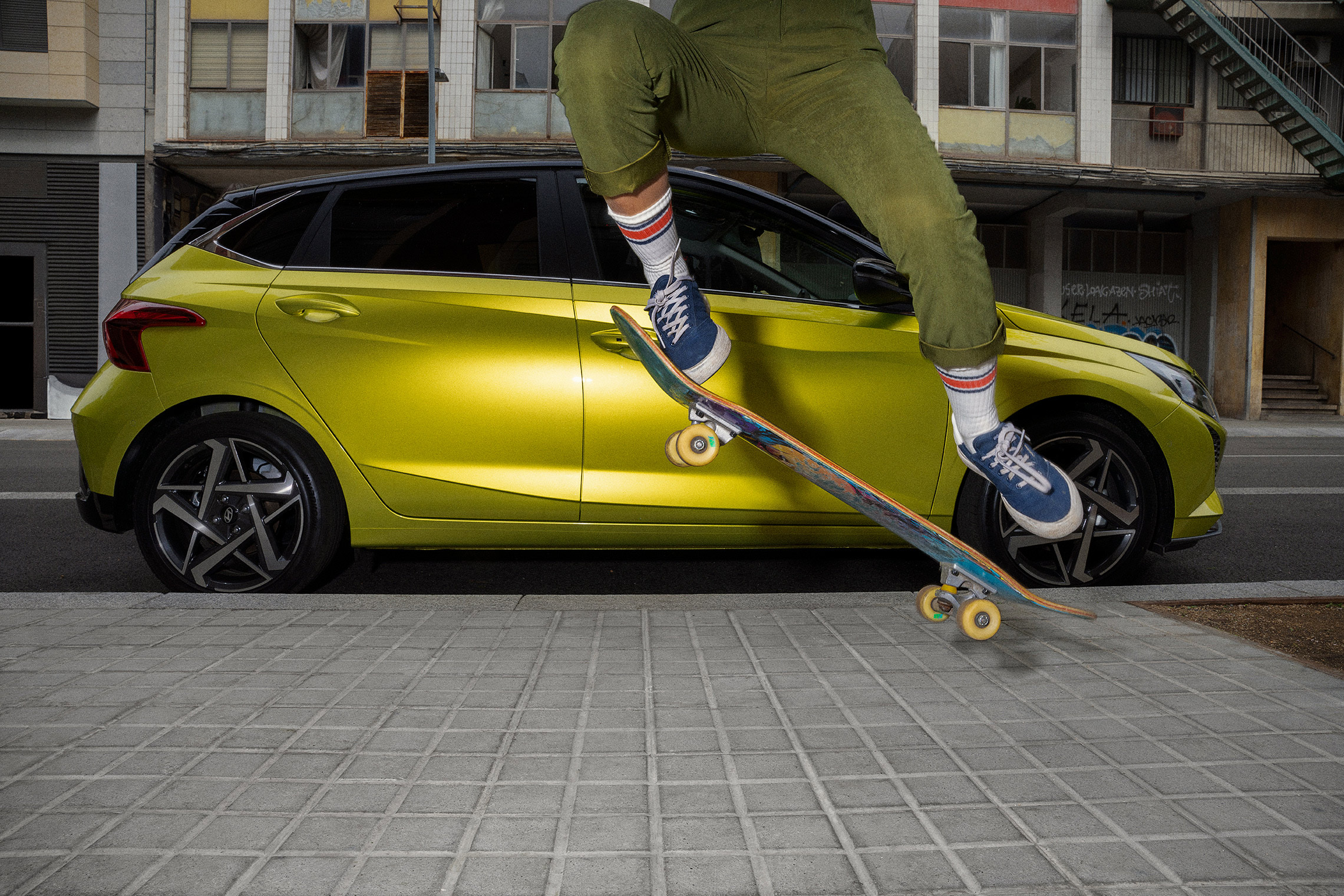 A young woman skateboarding in the street with a Hyundai i20 in the background.	