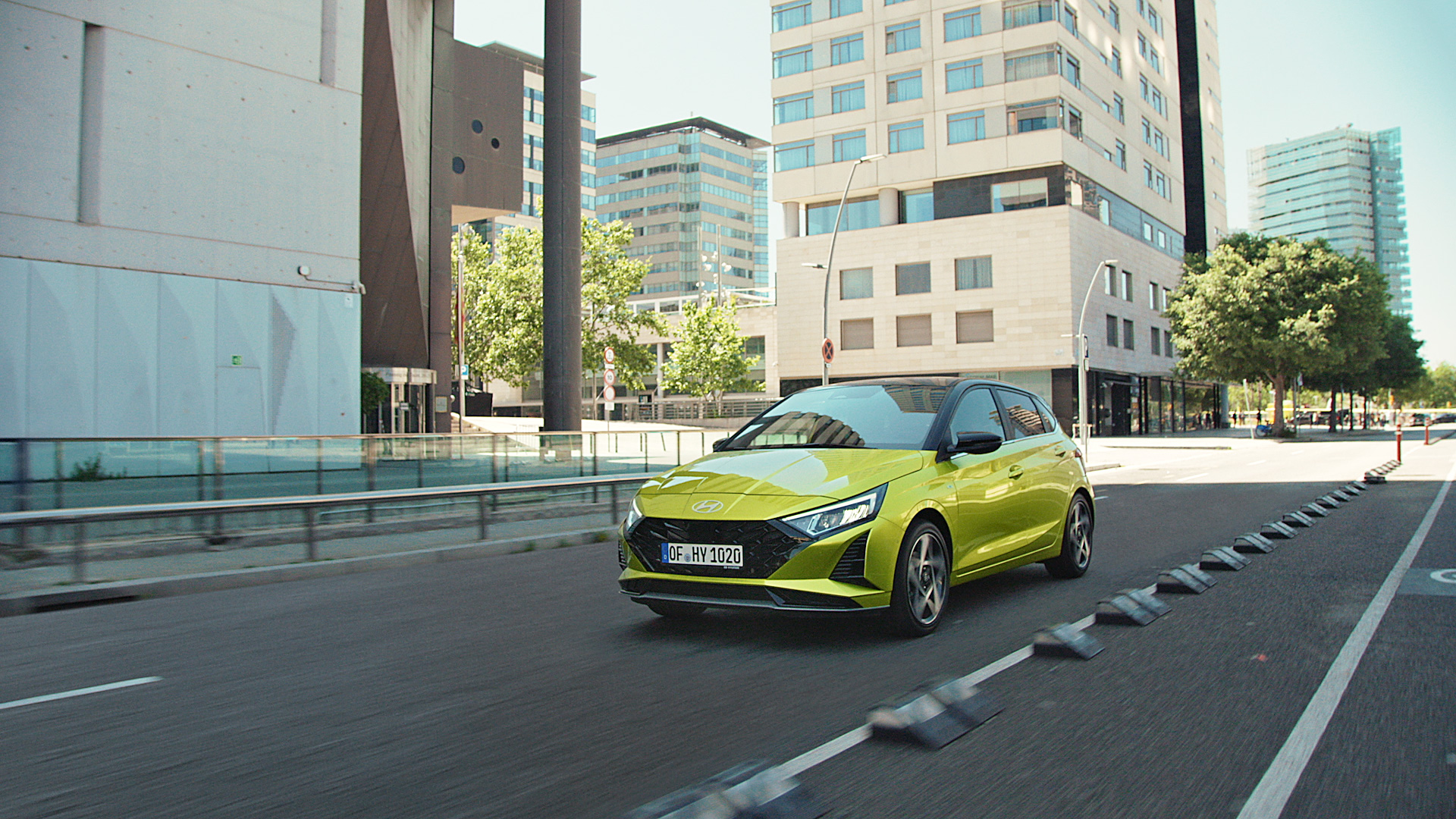 A green Hyundai i20 driving between modern building blocks.	