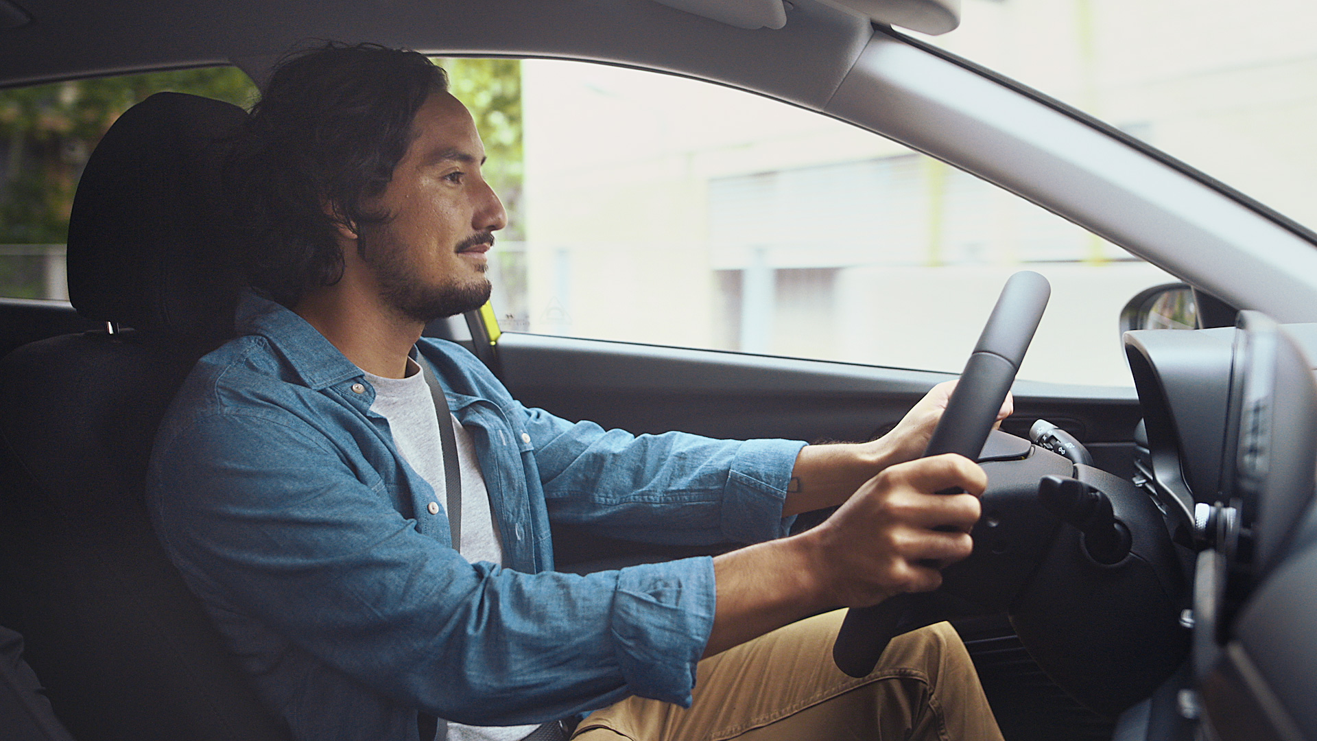 A young man in a blue shirt with his hands on the steering wheel of a Hyundai i20.	