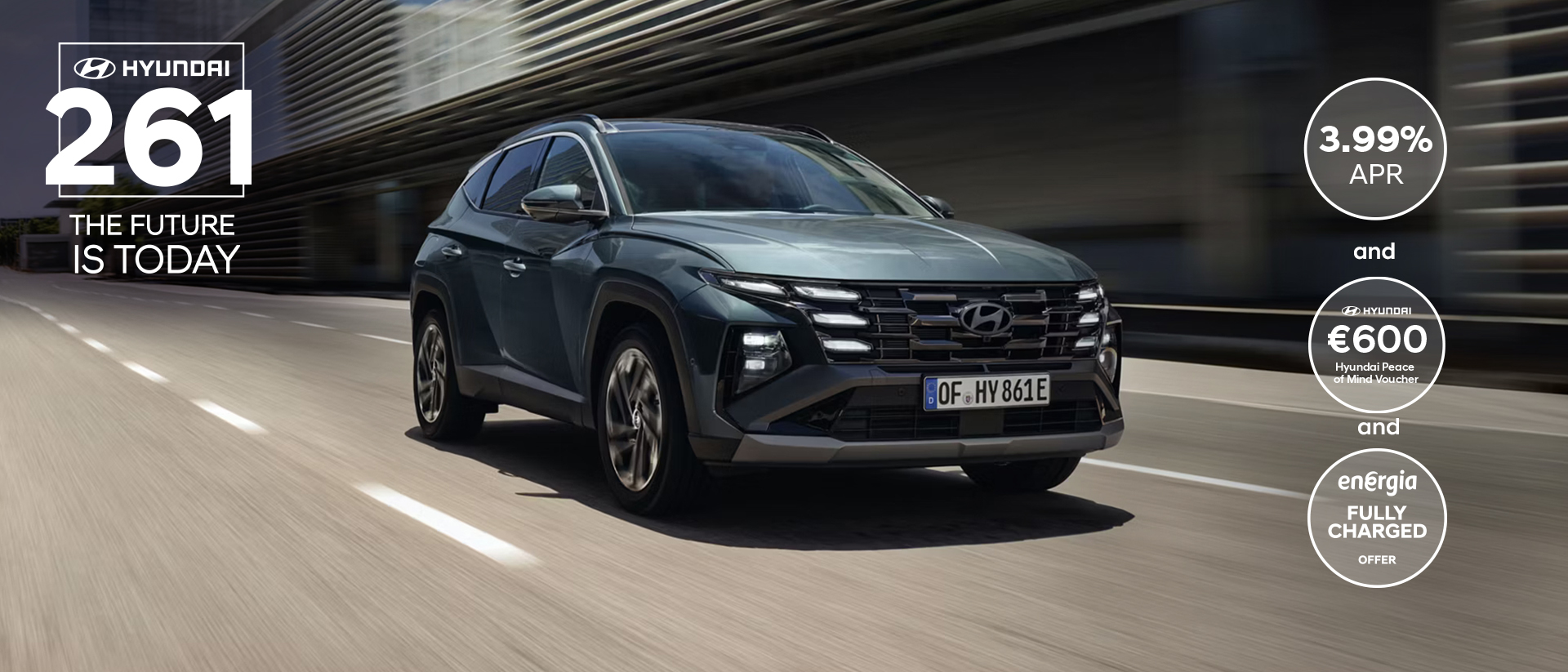 The Hyundai TUCSON Plug-in Hybrid driving down a city street with modern buildings visible.
