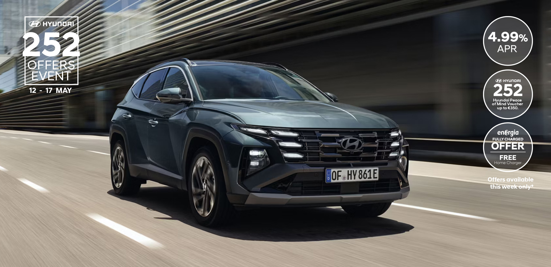 The Hyundai TUCSON Plug-in Hybrid driving down a city street with modern buildings visible.
