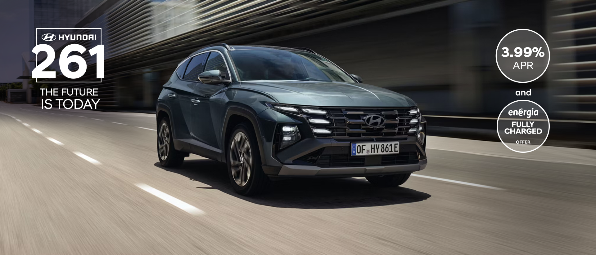 The Hyundai TUCSON Plug-in Hybrid driving down a city street with modern buildings visible.