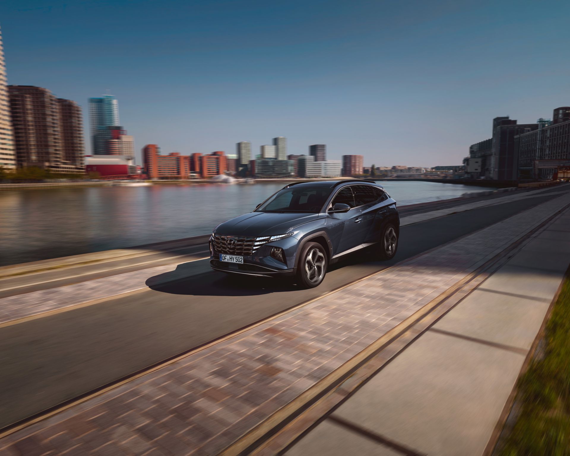 The All-New Hyundai Tucson compact SUV pictured from the rear parked near a waterfront skyline.