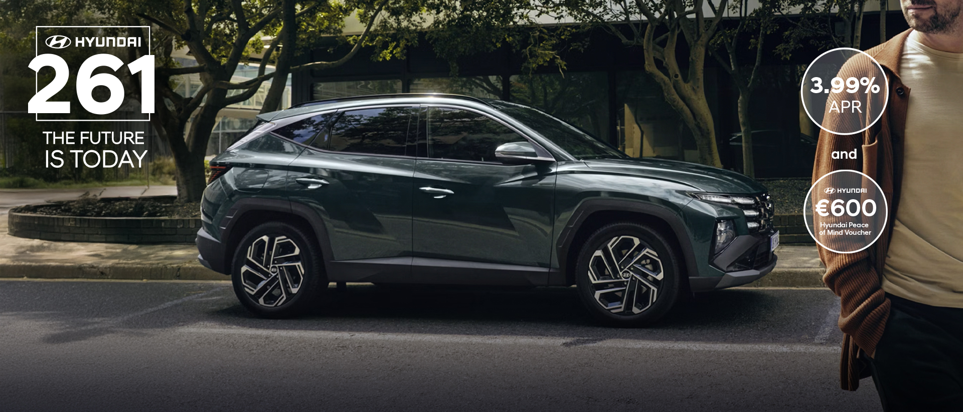 A man walking near a Hyundai&nbsp;TUCSON Hybrid parked by some trees.
